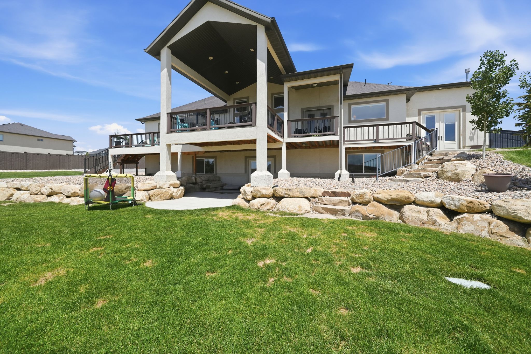 Spacious backyard with a vibrant lawn, stone retaining walls, and a multi-level deck system