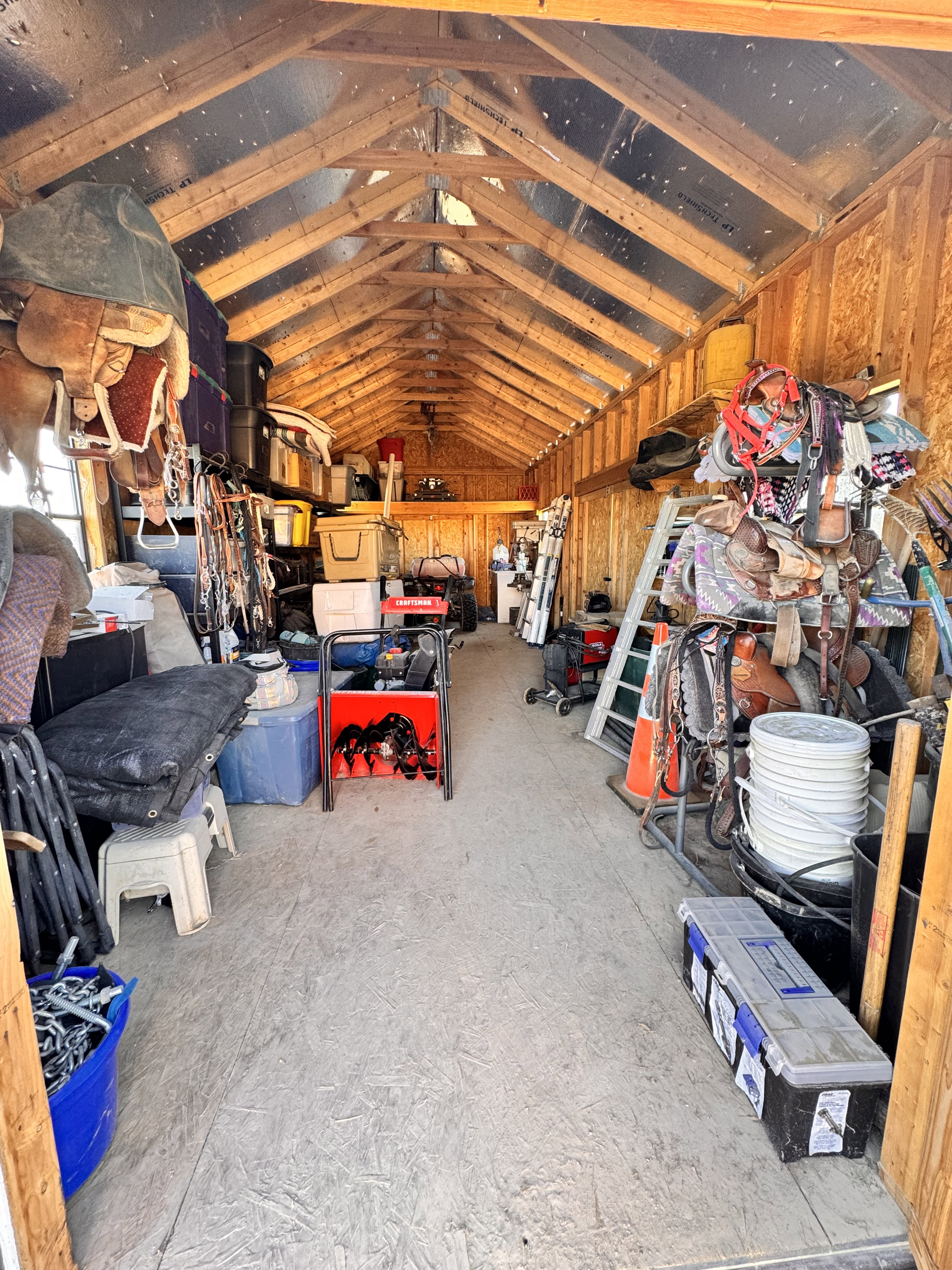 Spacious storage building featuring exposed wood framing, a high-pitched ceiling with reflective insulation, and durable wood-finish flooring
