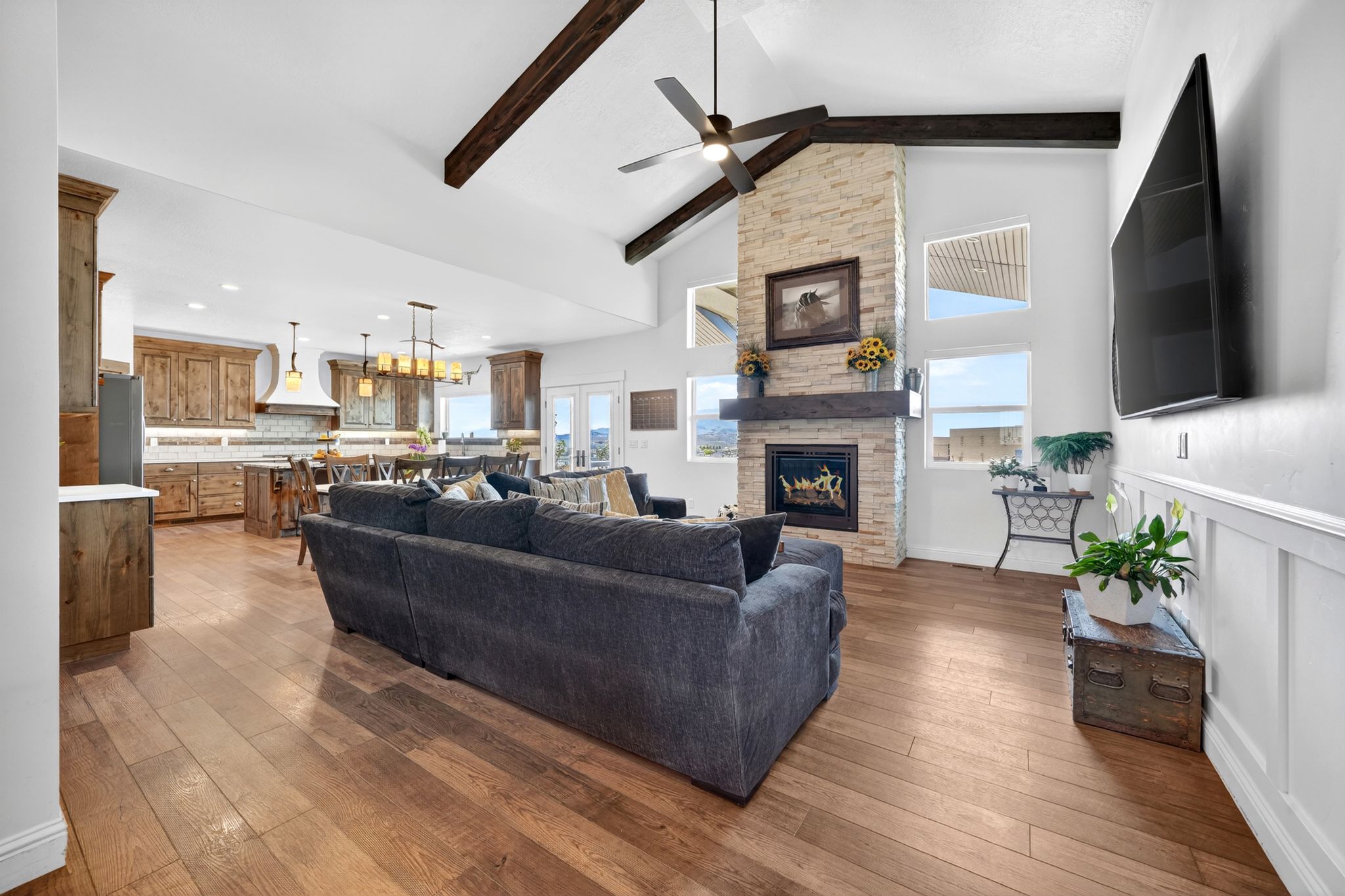 Spacious living area featuring high vaulted ceilings with exposed wood beams, a stone-front fireplace with a wood mantle, and wood-finish flooring