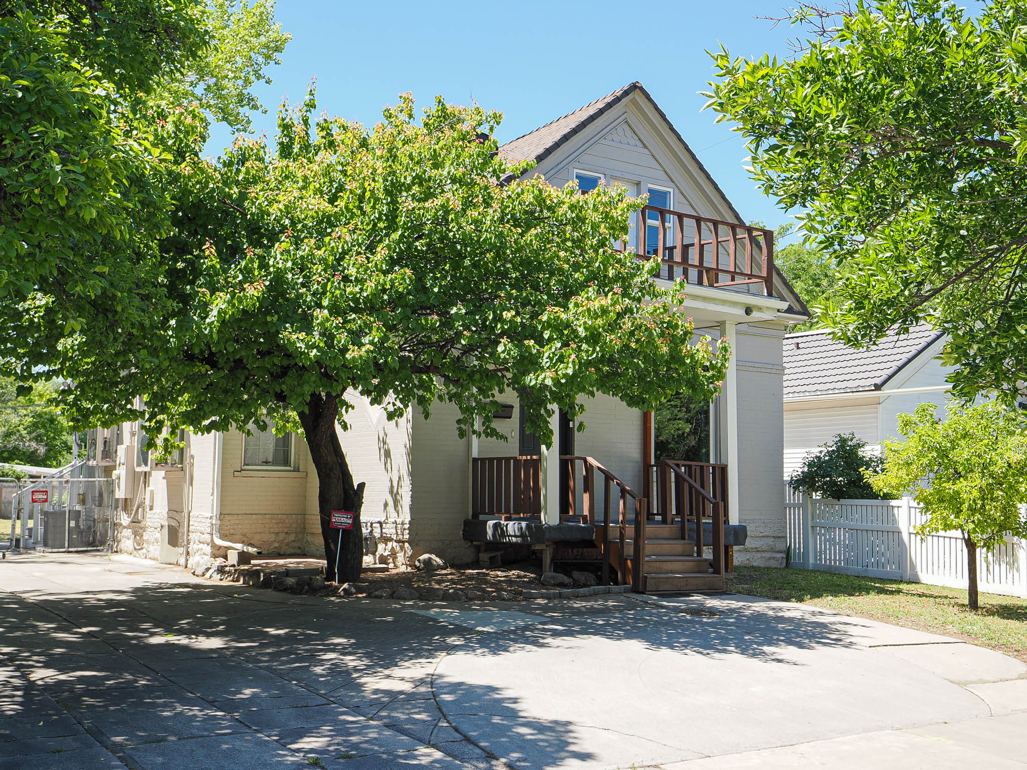 Gable roofline home featuring a second-story balcony with wood railing, covered entry with wood steps, and mature trees providing natural shade