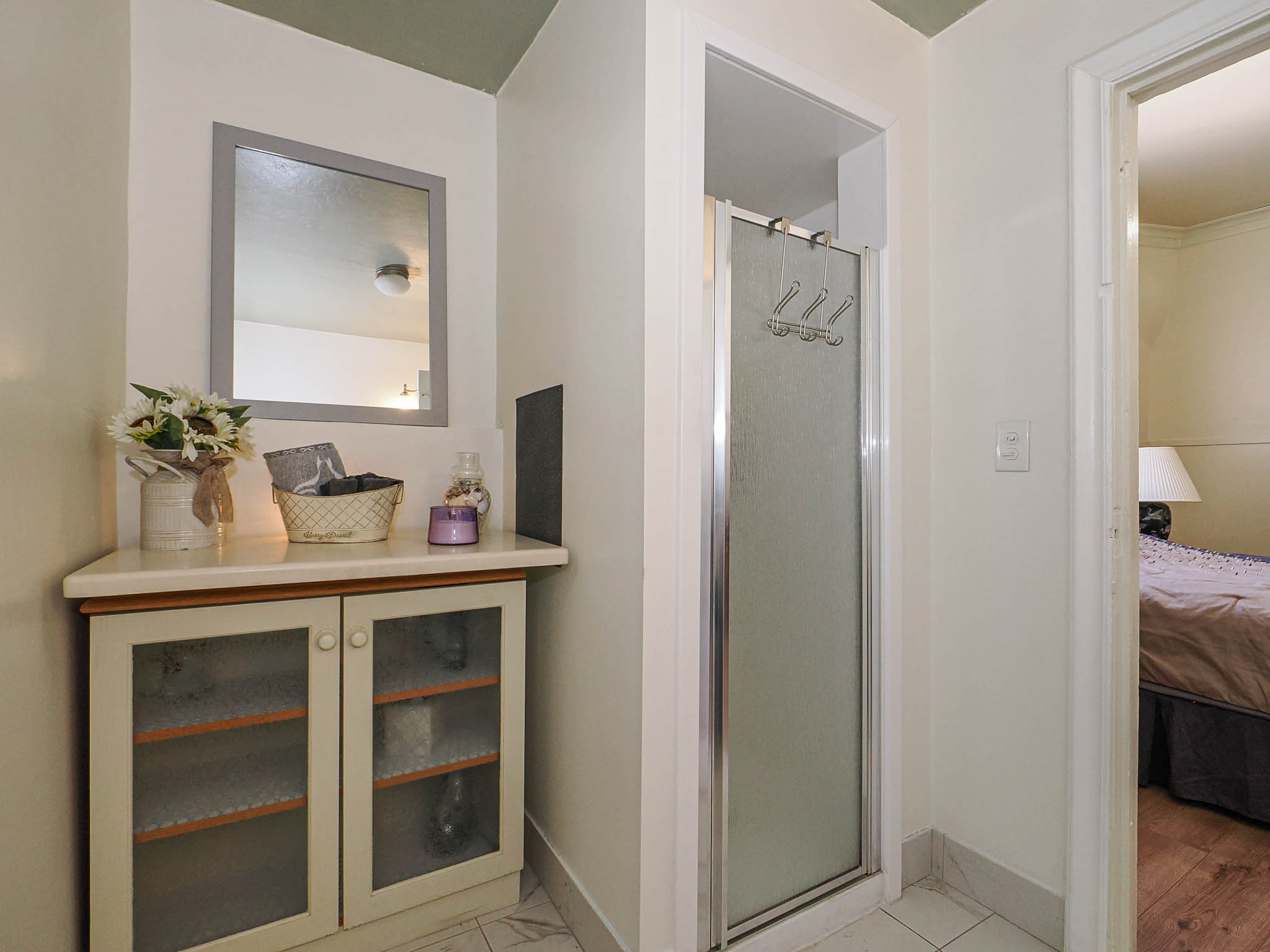 Compact bathroom featuring a glass-enclosed shower with a chrome frame, a built-in cabinet with glass-front doors, and a light-toned countertop