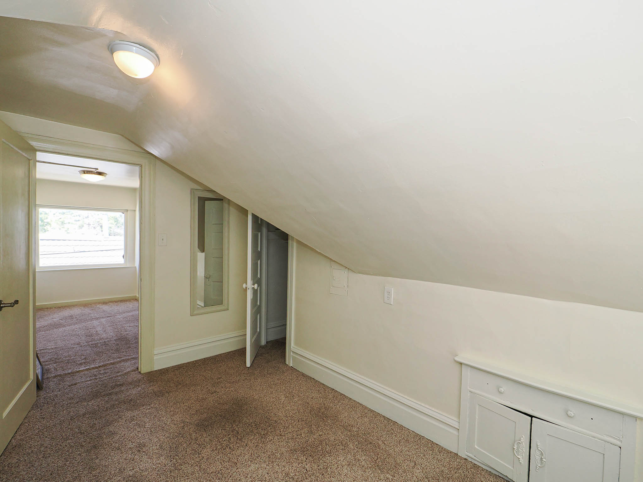 Sloped ceiling room featuring neutral carpet flooring, a flush-mount ceiling light, and built-in storage cabinetry