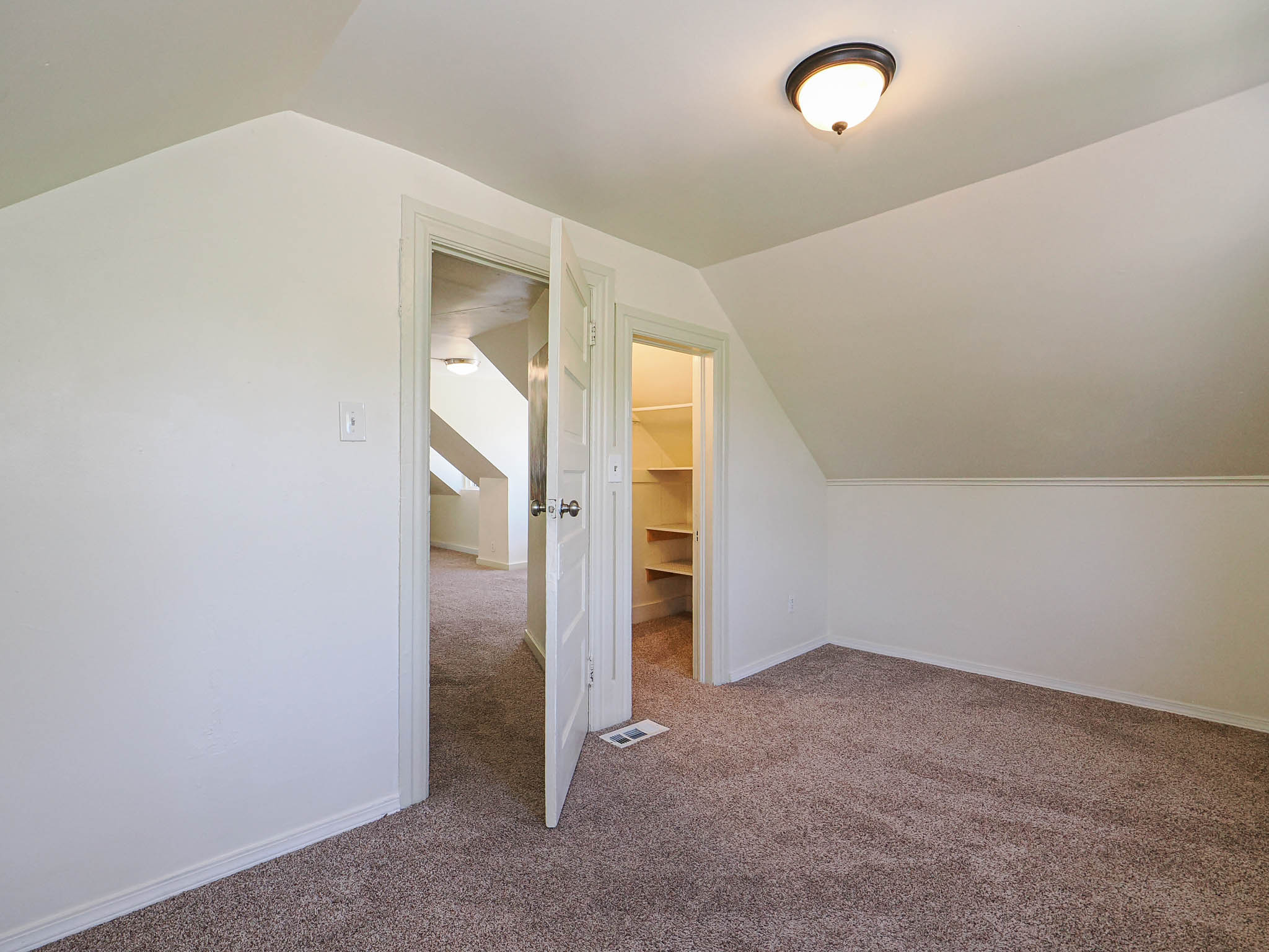 Attic space featuring sloped ceilings, a flush-mount ceiling light fixture, neutral carpet flooring, and a built-in closet with shelving