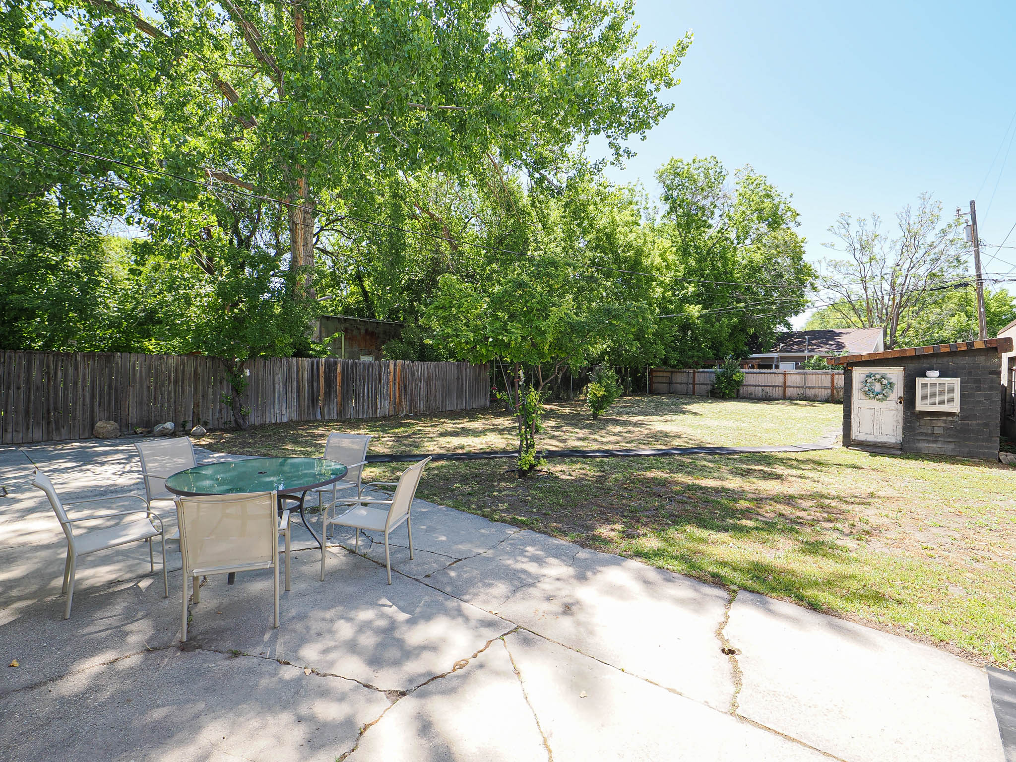 Expansive backyard featuring a concrete patio, a detached storage shed, and mature trees providing natural shade