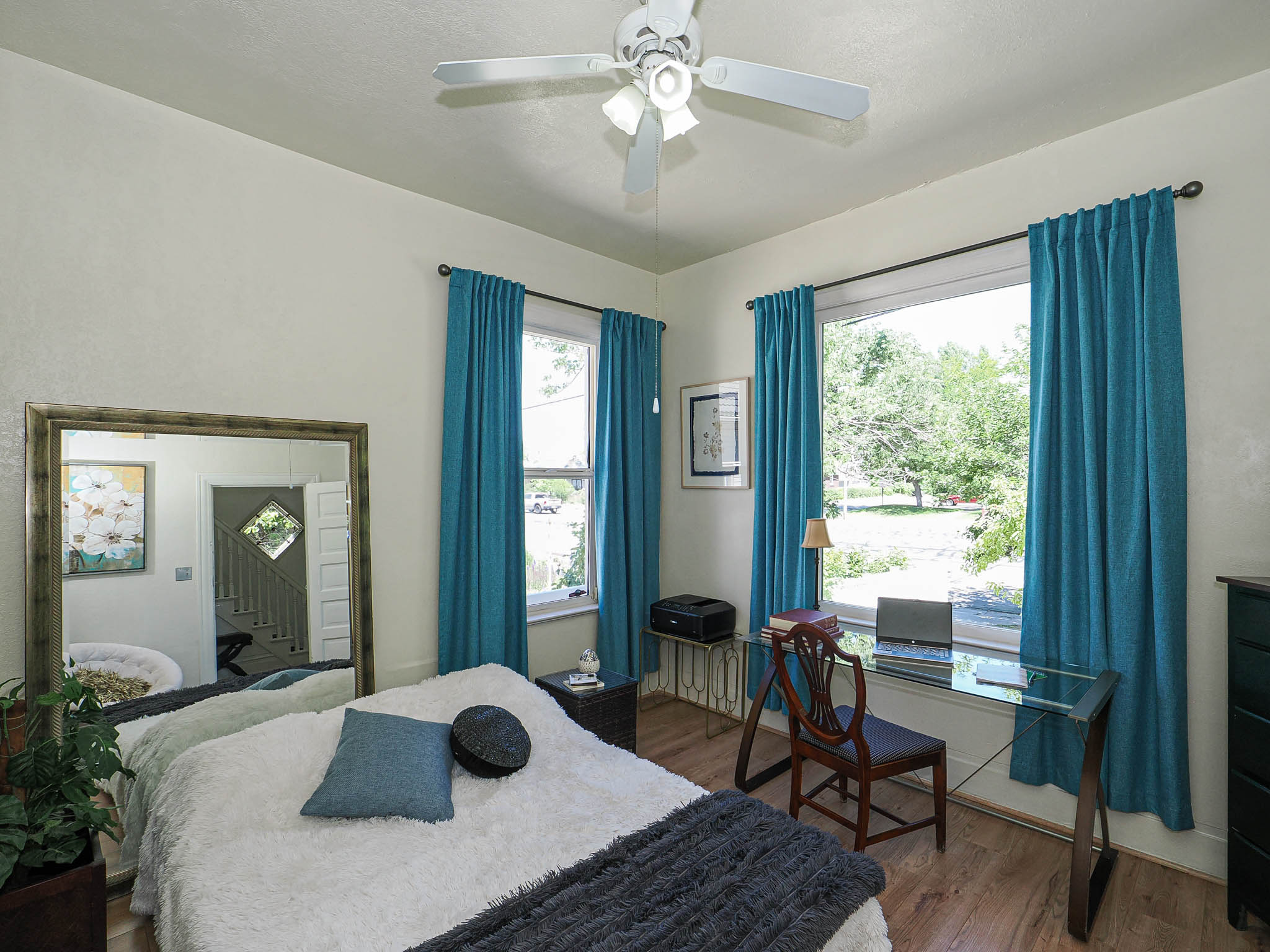 Bedroom featuring dual windows with vibrant teal drapes, wood-finish flooring, and a ceiling fan