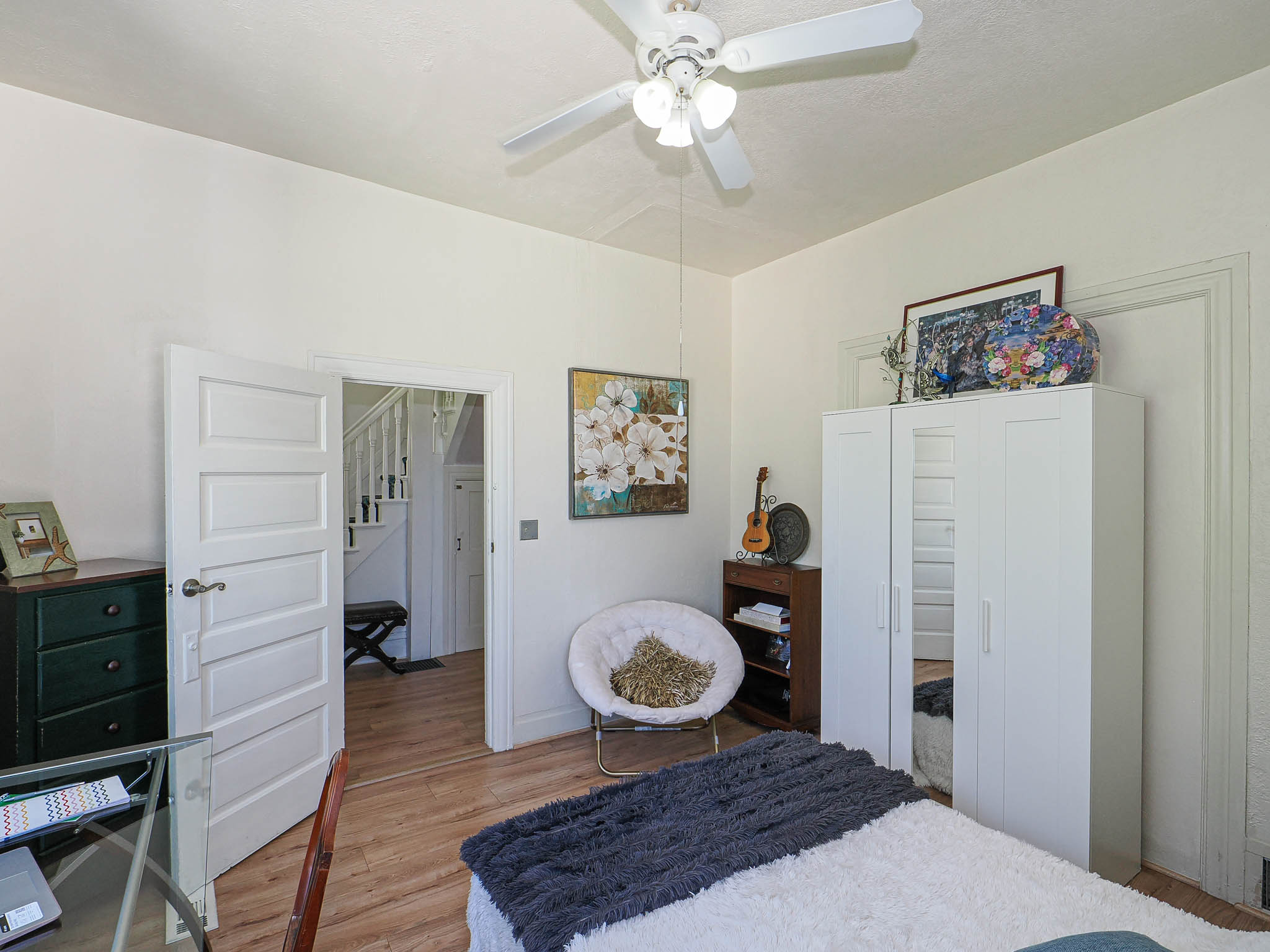 Room featuring wood-finish flooring, a ceiling fan with integrated lighting, white trim, and a paneled interior door