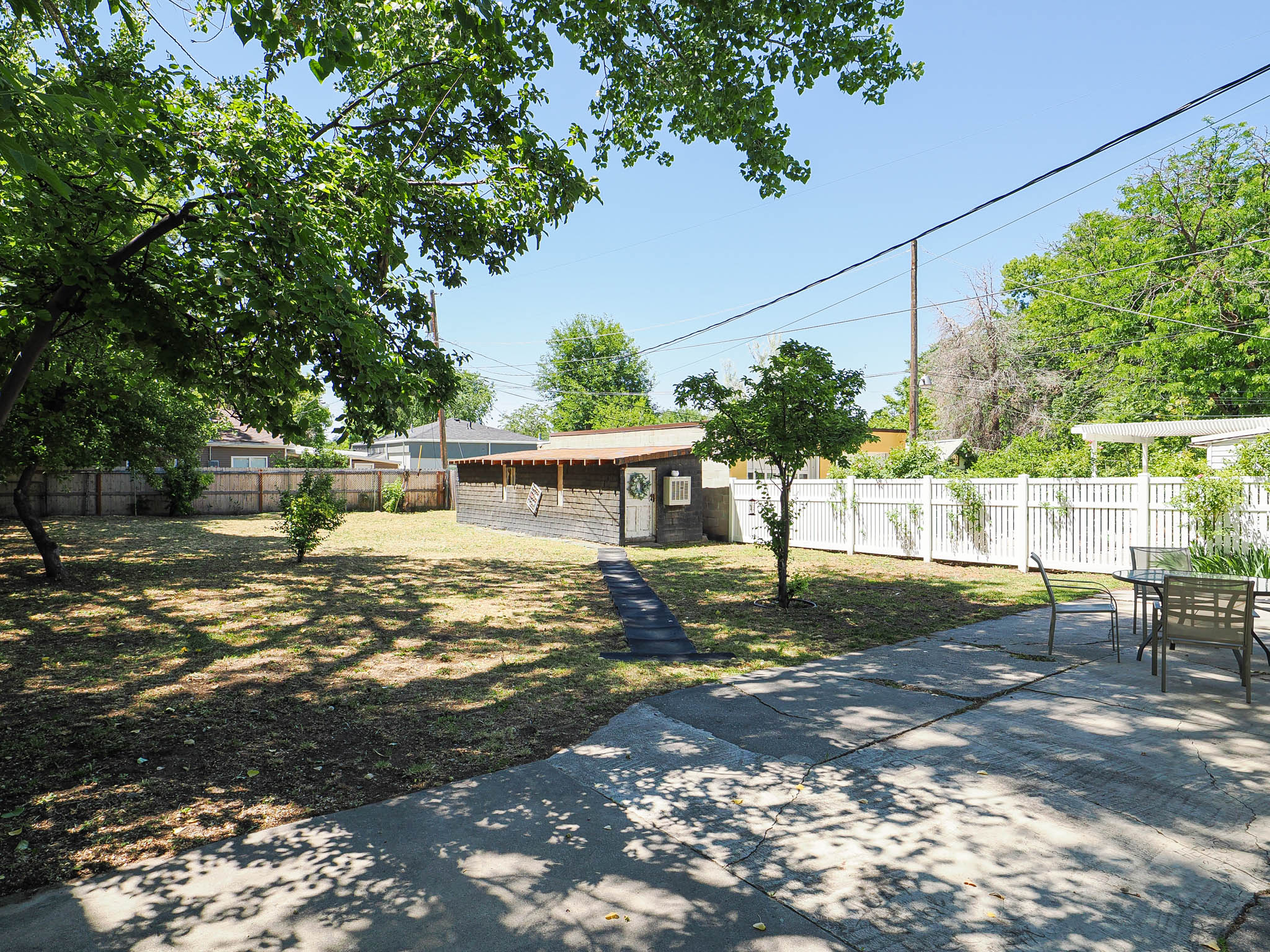 Expansive backyard featuring a concrete patio, a detached shed with wood-finish siding, a path of stepping stones, and a white picket fence