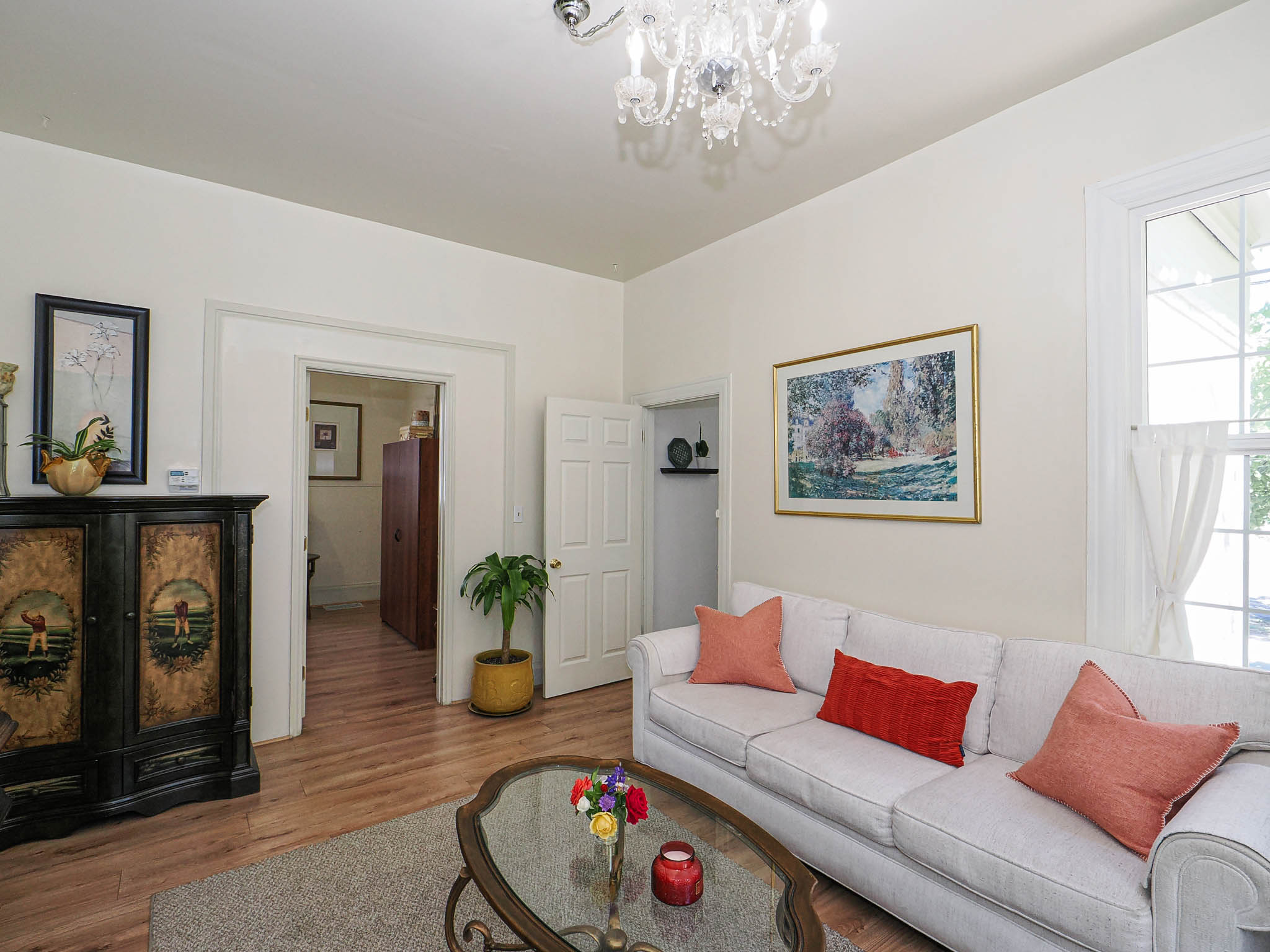 Living area featuring wood-finish flooring, a crystal chandelier, and a window with white trim
