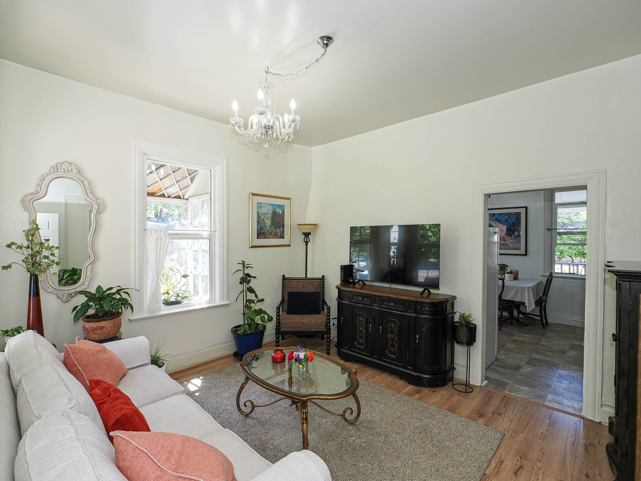 Living area featuring light wood-finish flooring, a decorative chandelier, white walls, and a large window with white trim