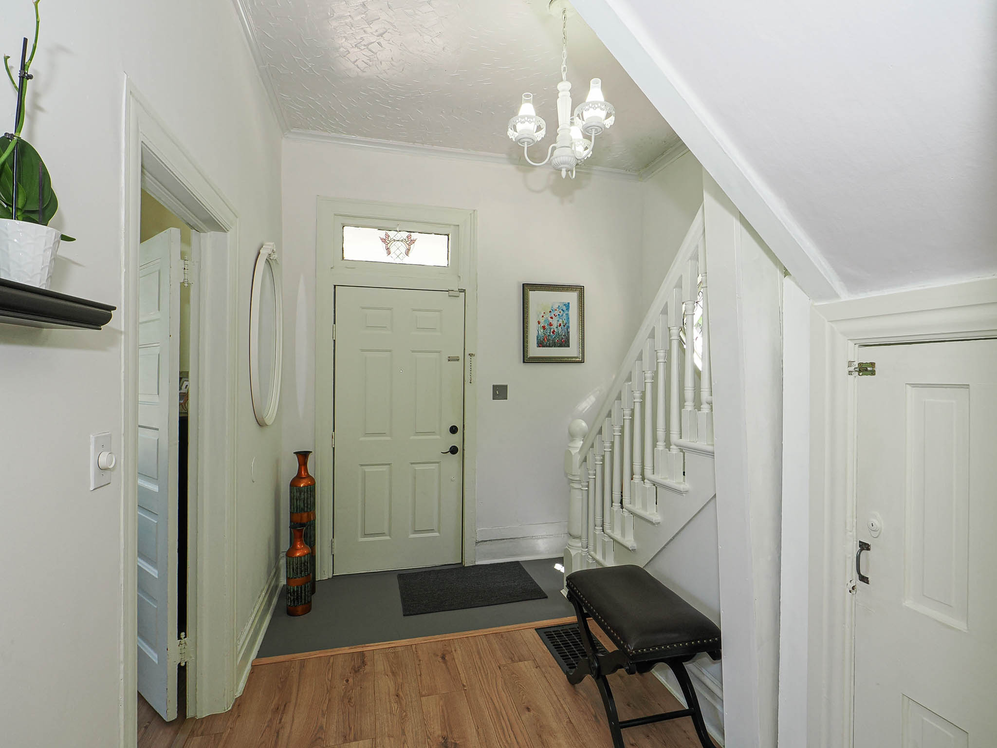Entryway featuring wood-finish flooring, a white paneled door with transom window, a white spindle staircase, and a white chandelier