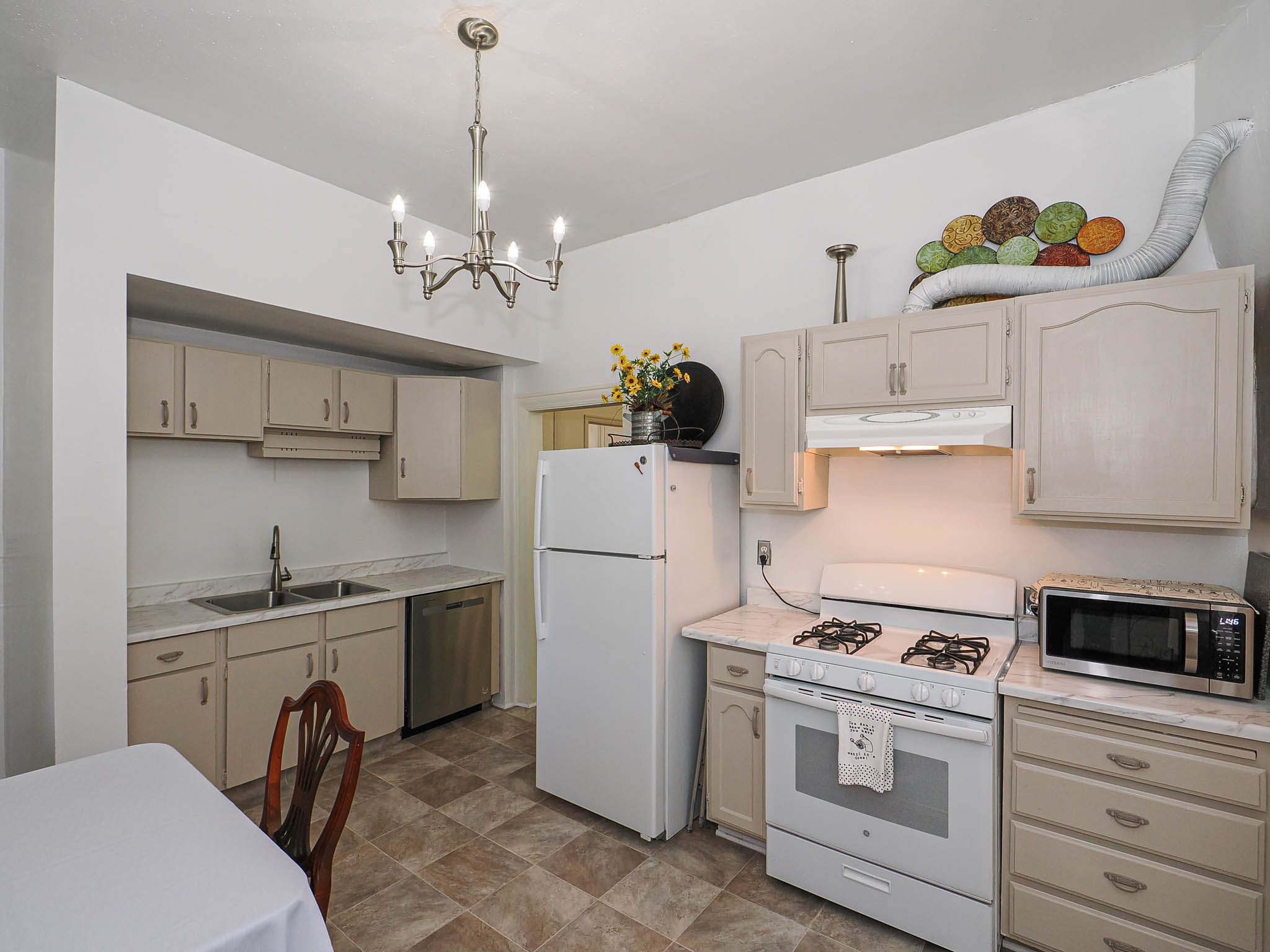 Kitchen featuring light-toned cabinetry, a double basin stainless steel sink, a stainless steel dishwasher, a white refrigerator, and a white gas range