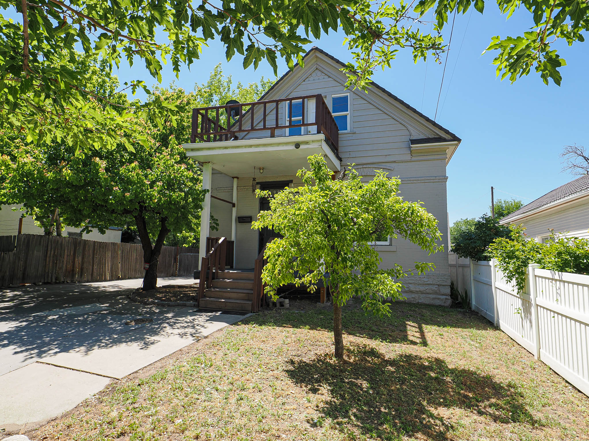 Two-story residence featuring light gray siding and a second-story balcony with wood railing