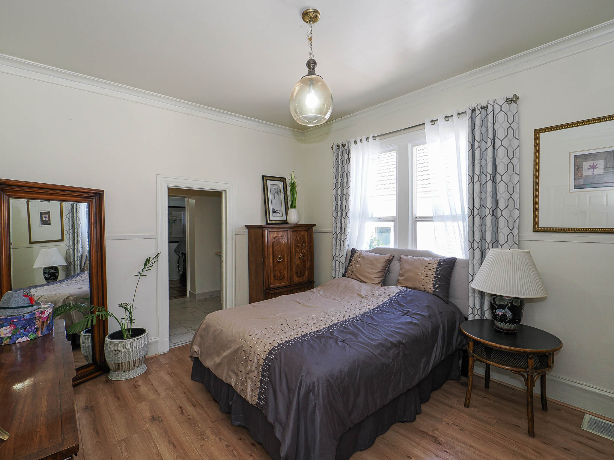 Wood-finish flooring throughout, featuring a window with white shutters, crown molding, and a paneled wall with a chair rail