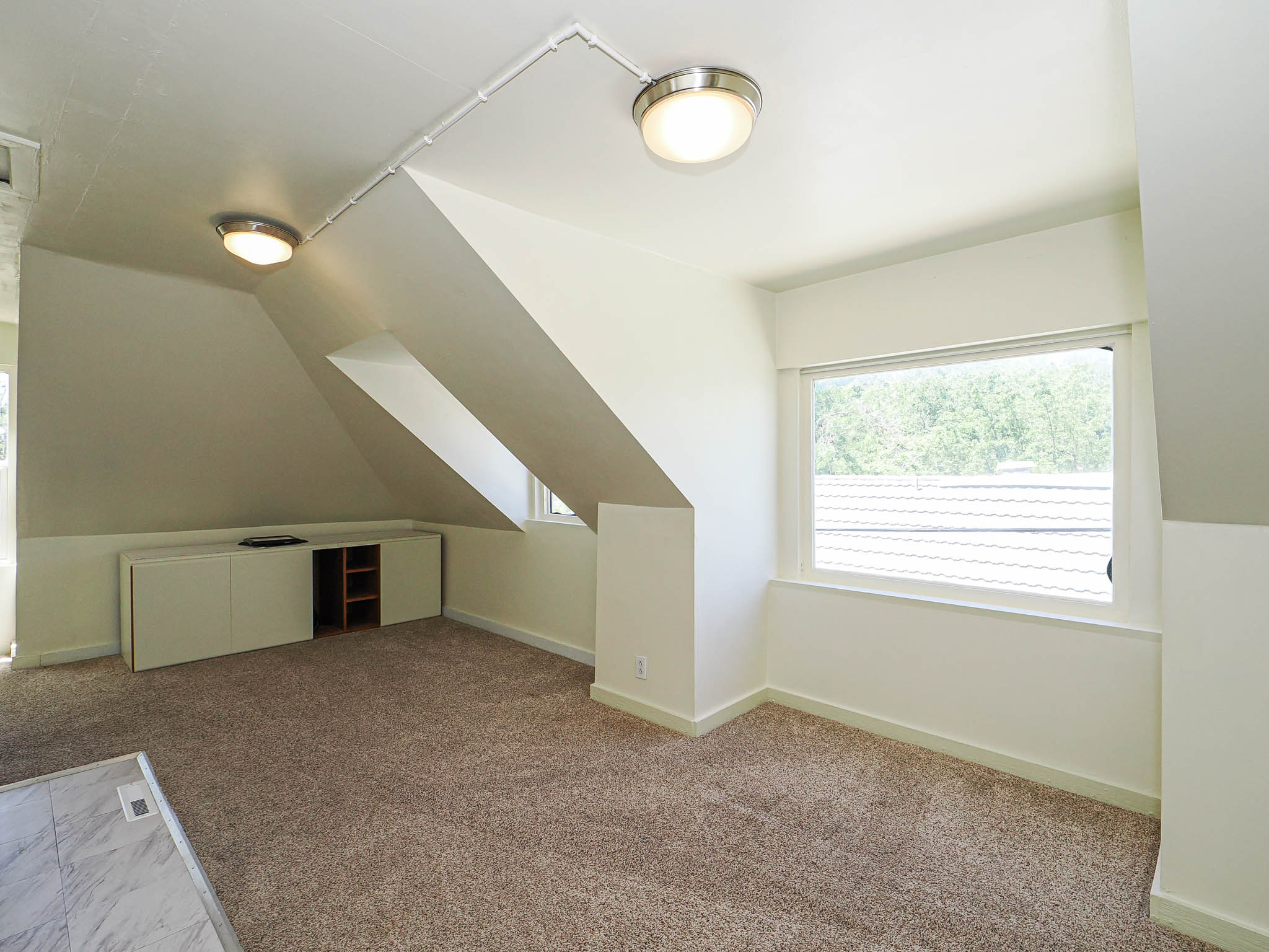 Carpeted room featuring built-in cabinetry with open shelving, multiple windows, two flush-mount ceiling lights, and sloped ceilings