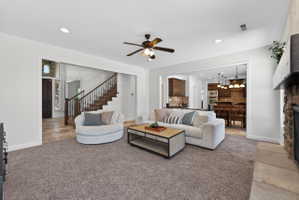Spacious living area featuring soft carpeting, a stone-faced fireplace with a substantial mantel, and a ceiling fan with integrated lighting