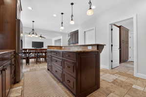 Kitchen island featuring dark wood cabinetry and a stone countertop with a tiled backsplash