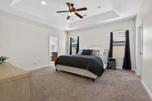Carpeted room featuring a tray ceiling with a ceiling fan, two windows with dark curtains, and an open doorway to another room