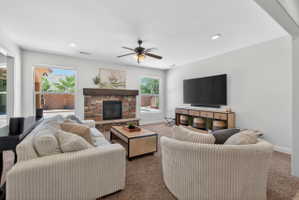 Living room featuring a stacked stone fireplace with a wood mantel, recessed lighting, and a ceiling fan