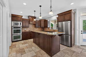 Well-appointed kitchen featuring rich wood cabinetry, granite countertops, stainless steel appliances, a tiled backsplash, and recessed lighting