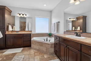 Soaking tub with stone surround, complemented by dual wood-finish vanities featuring light-toned countertops and integrated sinks