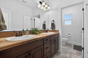Dual vanity featuring undermount sinks, bronze finish faucets, and a light brown countertop with a tiled backsplash