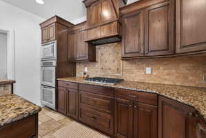 Gourmet kitchen featuring custom wood cabinetry, granite countertops, tile backsplash, and stainless steel built-in appliances including a double oven and microwave