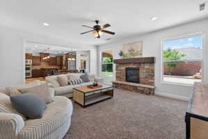 Spacious living area featuring a stone-clad fireplace with a wood mantel, an open concept layout, recessed lighting, a ceiling fan, and large windows