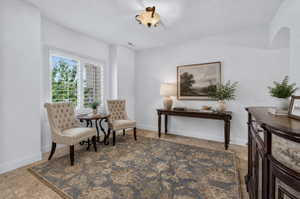 Bright interior space featuring a window with plantation shutters, tile flooring, and an arched doorway