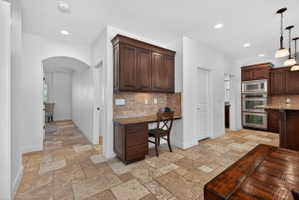 Built-in desk area with dark wood cabinetry, granite countertop, and tiled backsplash