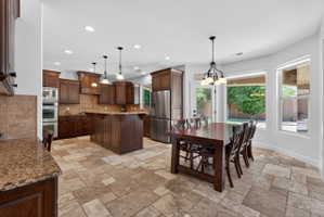 Spacious kitchen and dining area with stone tile flooring, rich wood cabinetry, stainless steel appliances, and a central island