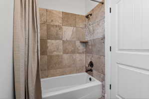 Tub-shower combination featuring bronze fixtures, earth-toned tile surround, and a built-in shelf