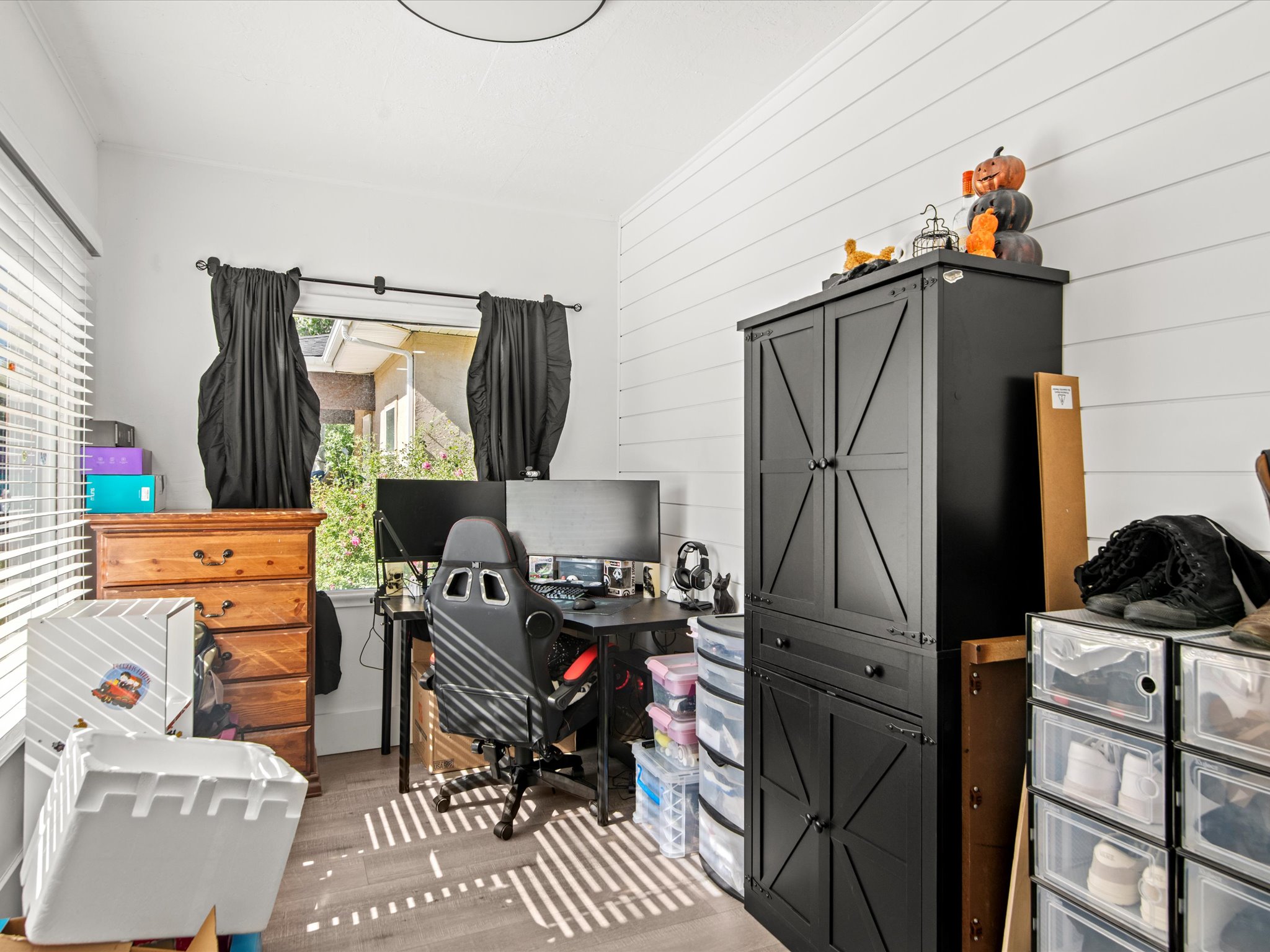 Bright room featuring white shiplap accent wall, wood-finish flooring, and a large window with blinds