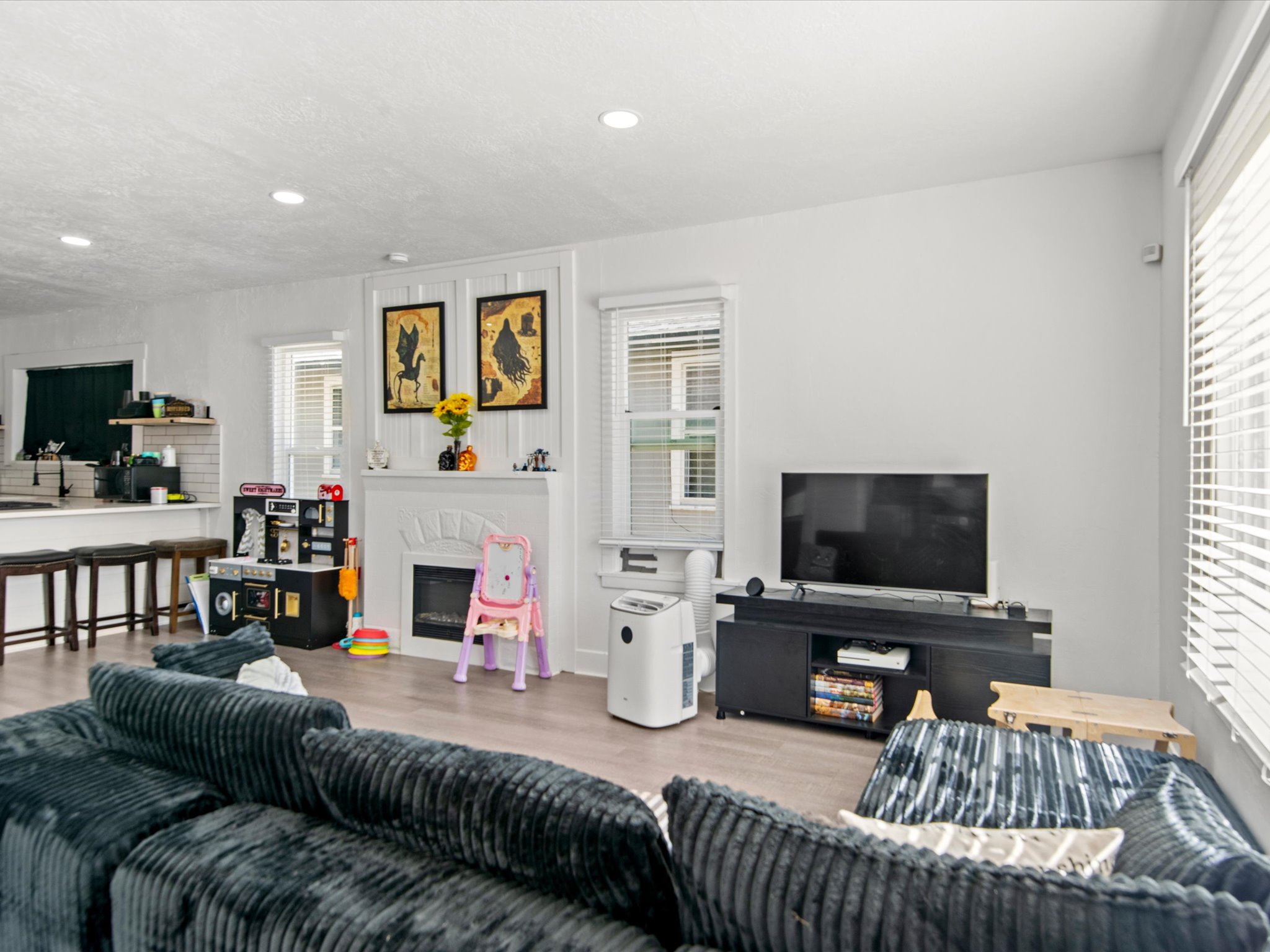 Open-concept living space featuring light wood-finish flooring, recessed lighting, and a white fireplace with a decorative mantel and hearth