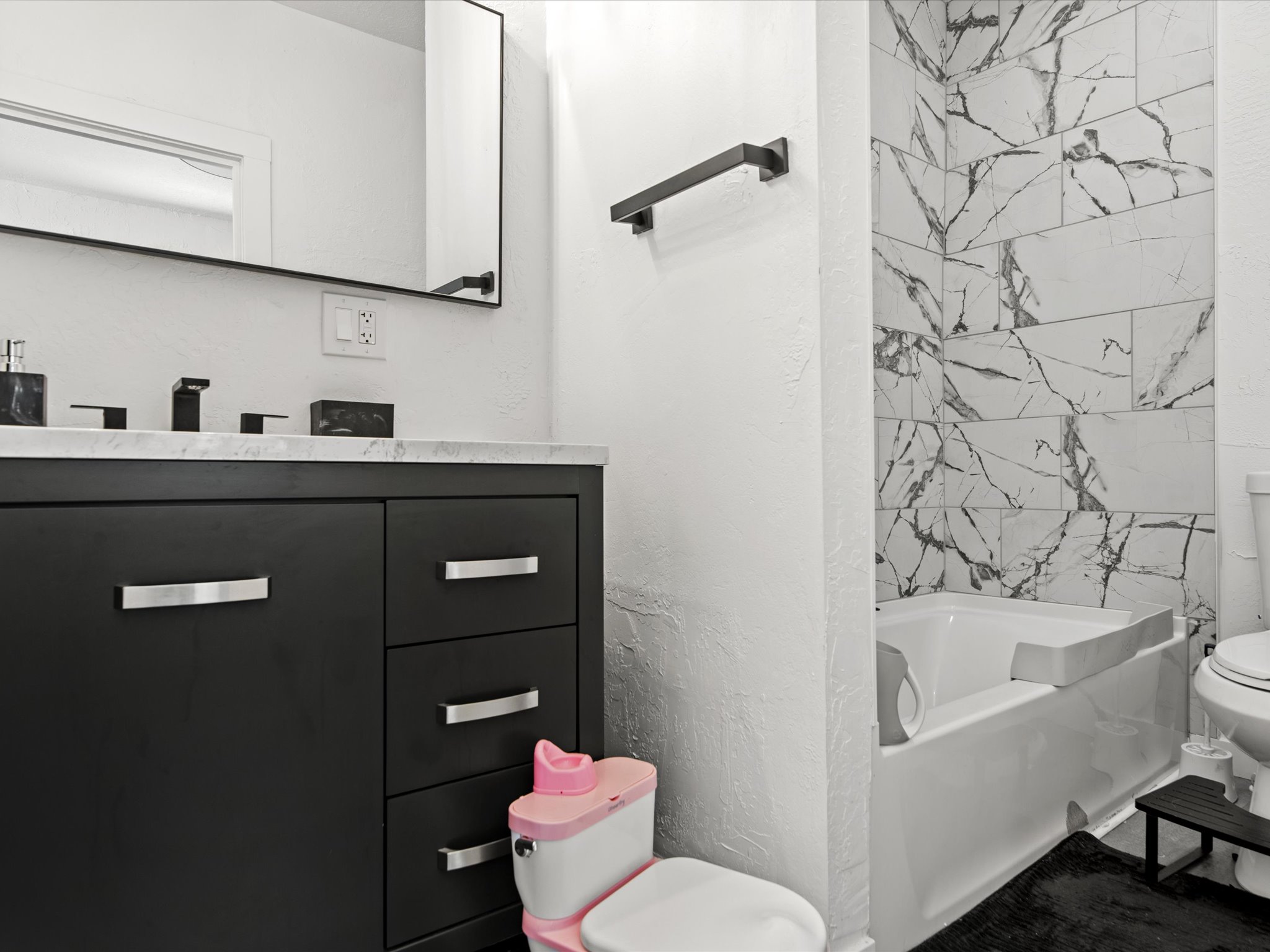 Bathroom featuring a dark wood vanity with a light-toned countertop, a rectangular mirror with a black frame, black fixtures, and a white tiled shower surround with dark veining