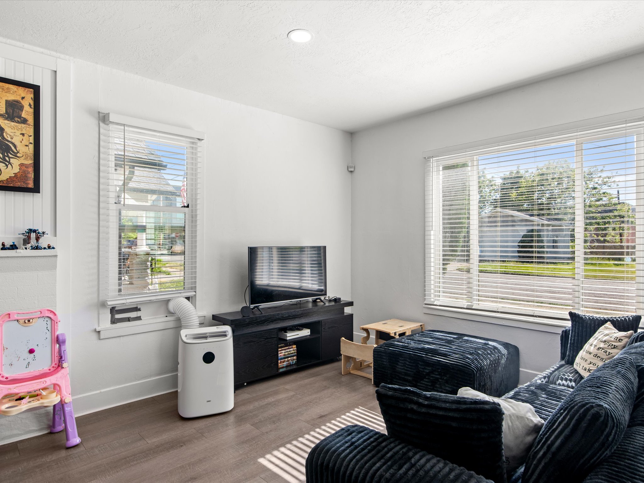 Living area featuring wood-finish flooring, white walls, recessed ceiling lighting, and multiple windows with blinds