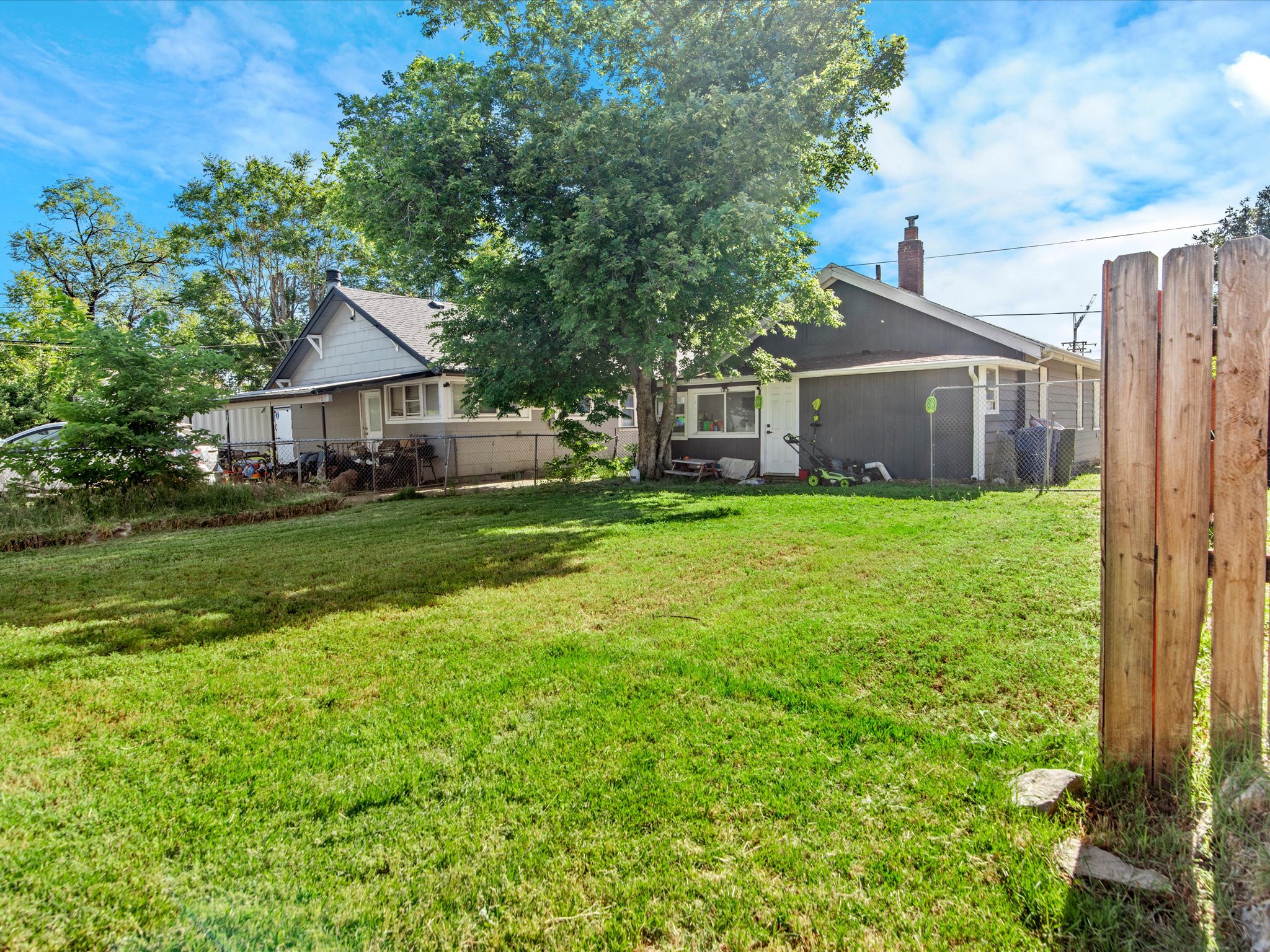 Expansive grassy yard with mature trees and a partial wood privacy fence