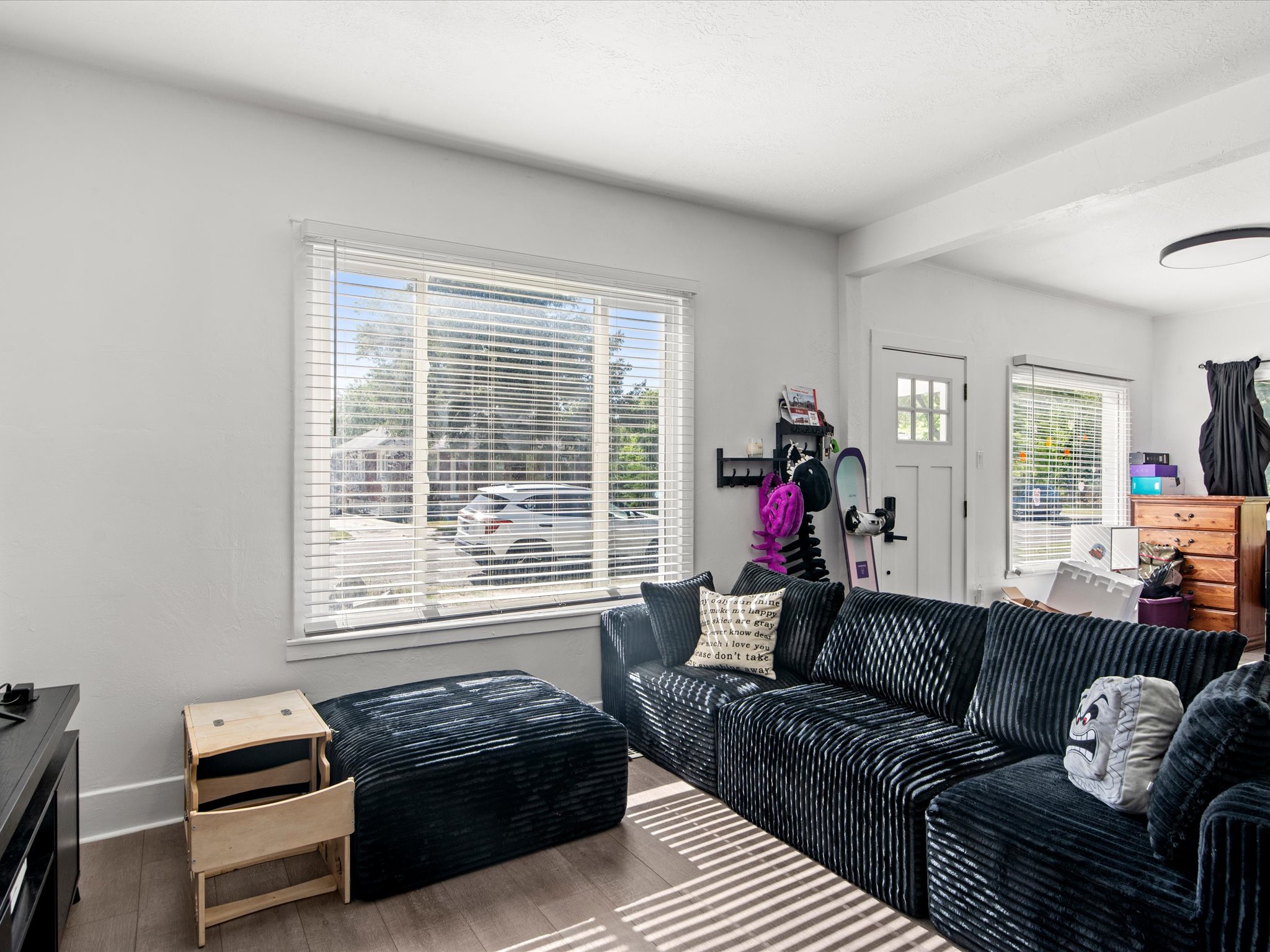 Living area featuring wood-finish flooring, white baseboards, and a large window with blinds