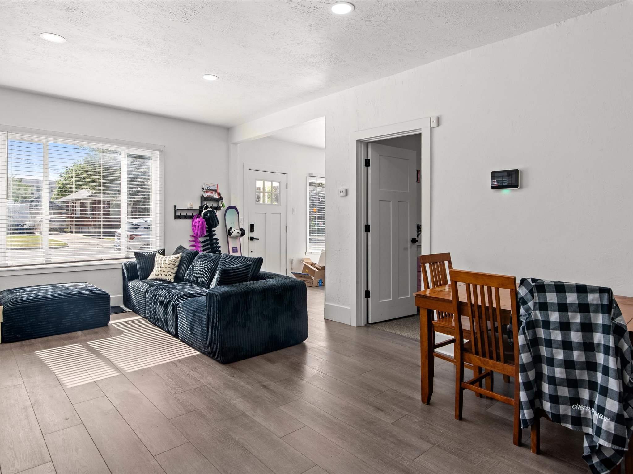 Spacious living area featuring light wood-finish flooring, recessed lighting, and a large window with blinds