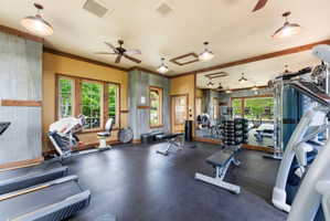 Dedicated fitness room featuring rubber flooring, multiple windows with wood-finish trim, a full-wall mirror, industrial-style pendant lighting, and ceiling fans