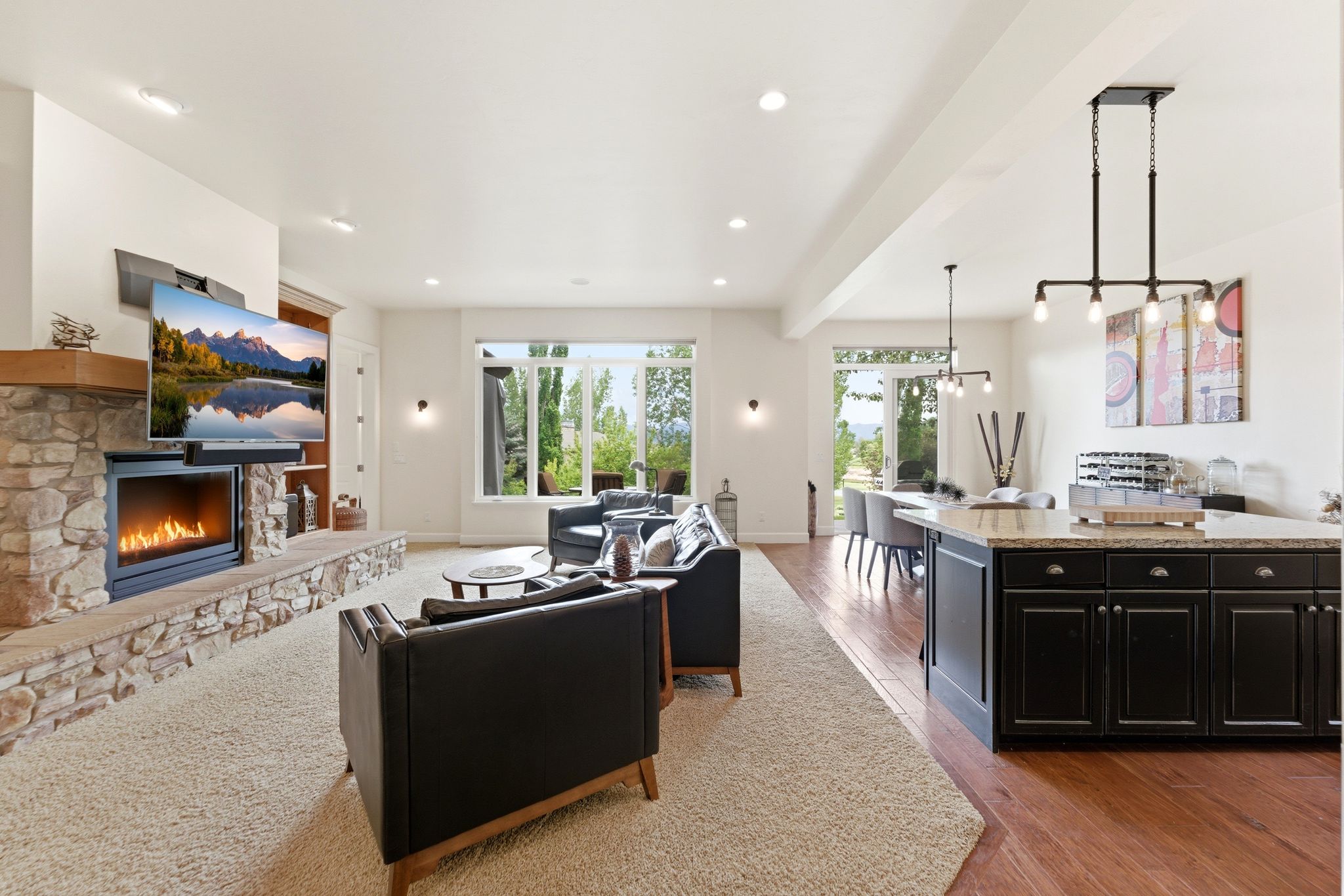 Spacious living area featuring a stone fireplace with a wood mantle, large windows, recessed lighting, and mixed flooring with carpet and wood-finish