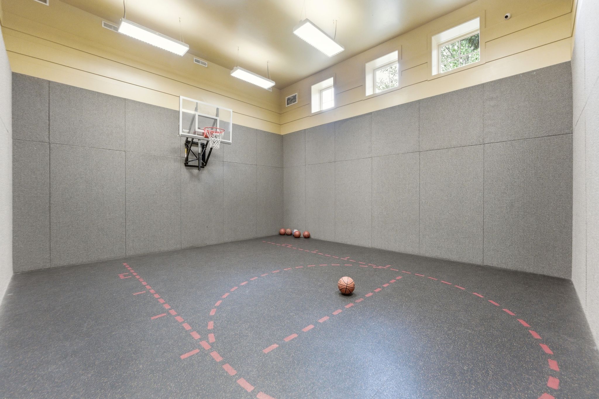 Indoor sports court featuring a basketball hoop, cushioned wall panels, and a marked court surface