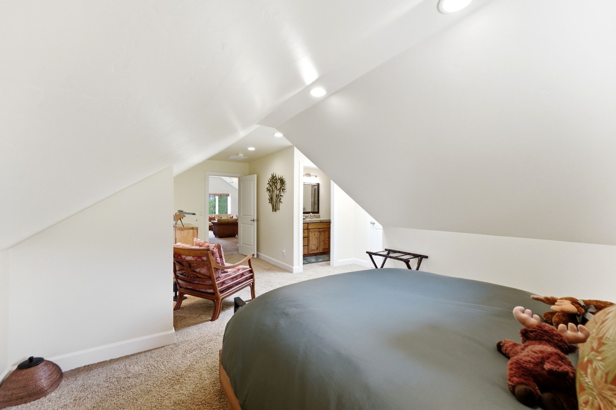 Carpeted attic space featuring sloped ceilings, recessed lighting, and a doorway opening to an additional room