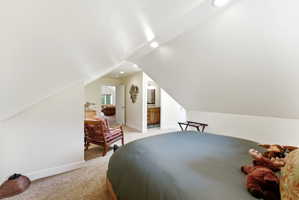 Carpeted attic space featuring sloped ceilings, recessed lighting, and a doorway opening to an additional room