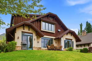 Exterior featuring a stucco and wood-paneled facade, stone accents, multiple large windows, a patio area, and a sloped lawn