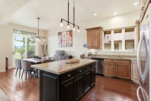 Open-concept kitchen and dining area featuring wood-finish flooring, a dark kitchen island with a light-toned countertop, a kitchen perimeter with wood cabinetry and a light-toned countertop, and a dining area with a glass slider