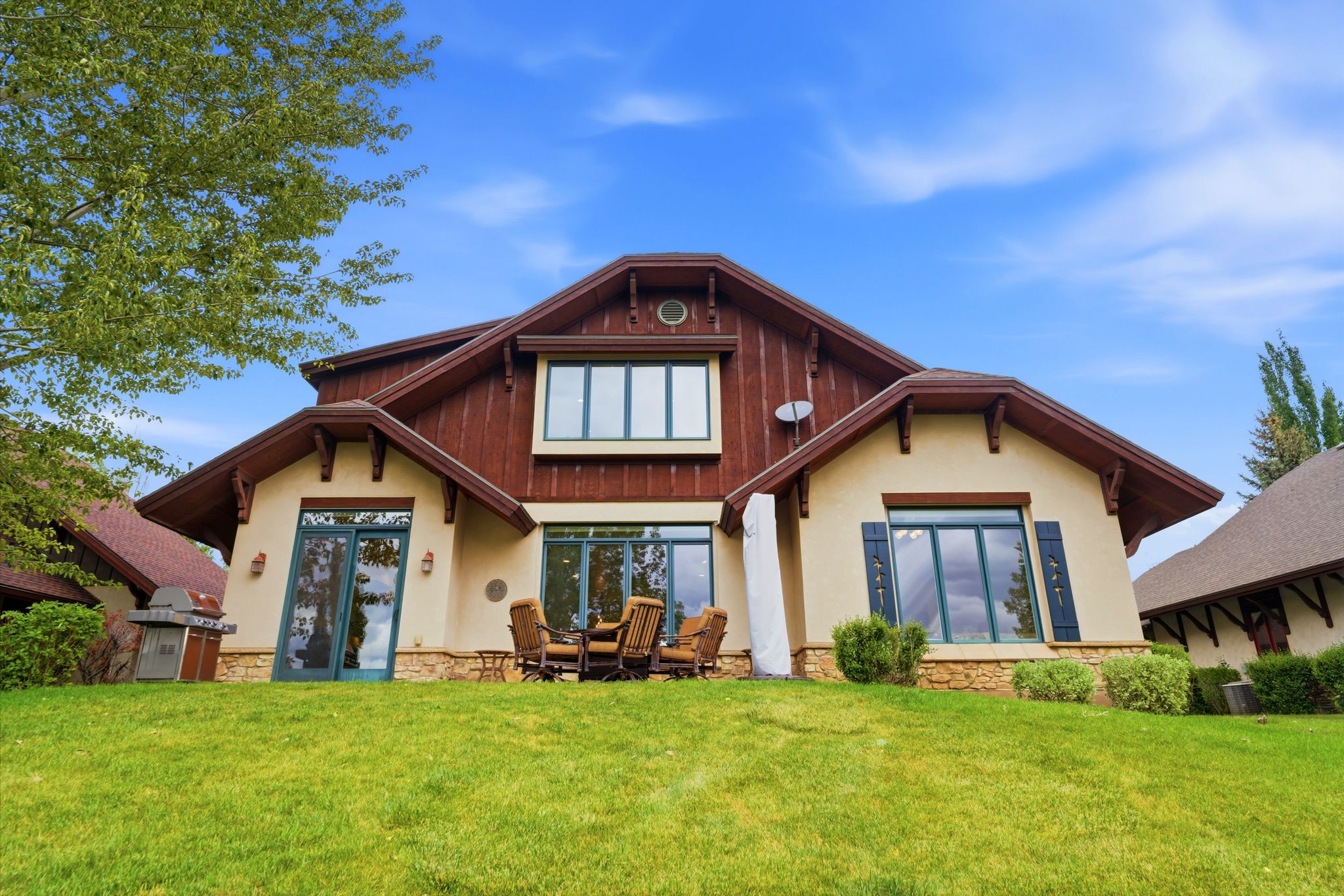 Rear exterior featuring a stone foundation, stucco siding, dark wood accents, and a patio with direct access to the lawn