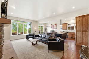 Open-concept living space featuring a stone fireplace with a wood mantle, a wall of windows, recessed lighting, and wood-finish flooring in the kitchen and dining areas