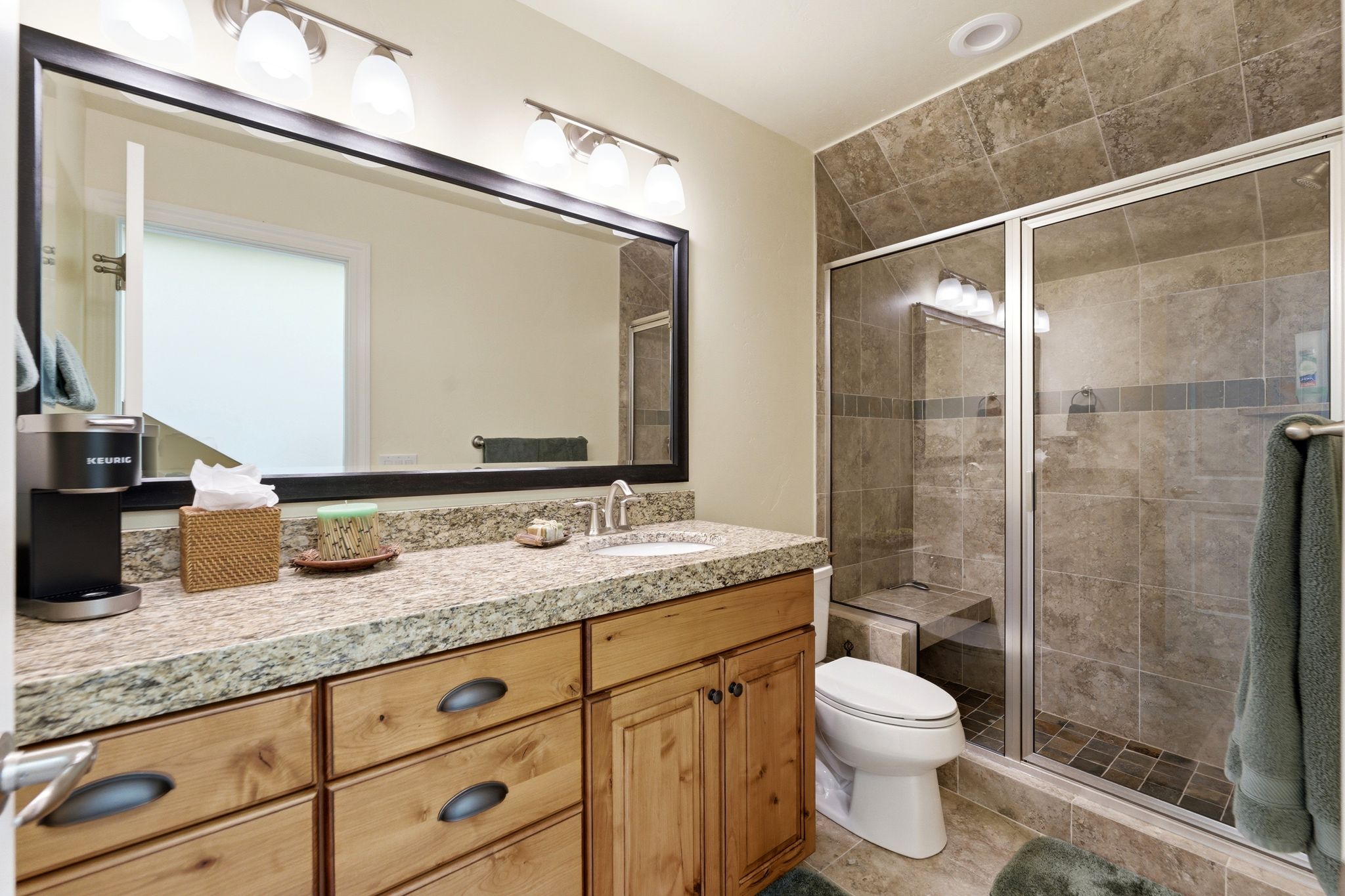 Bathroom featuring a wood-finish vanity with a light-toned countertop, an integrated sink, and a large framed mirror