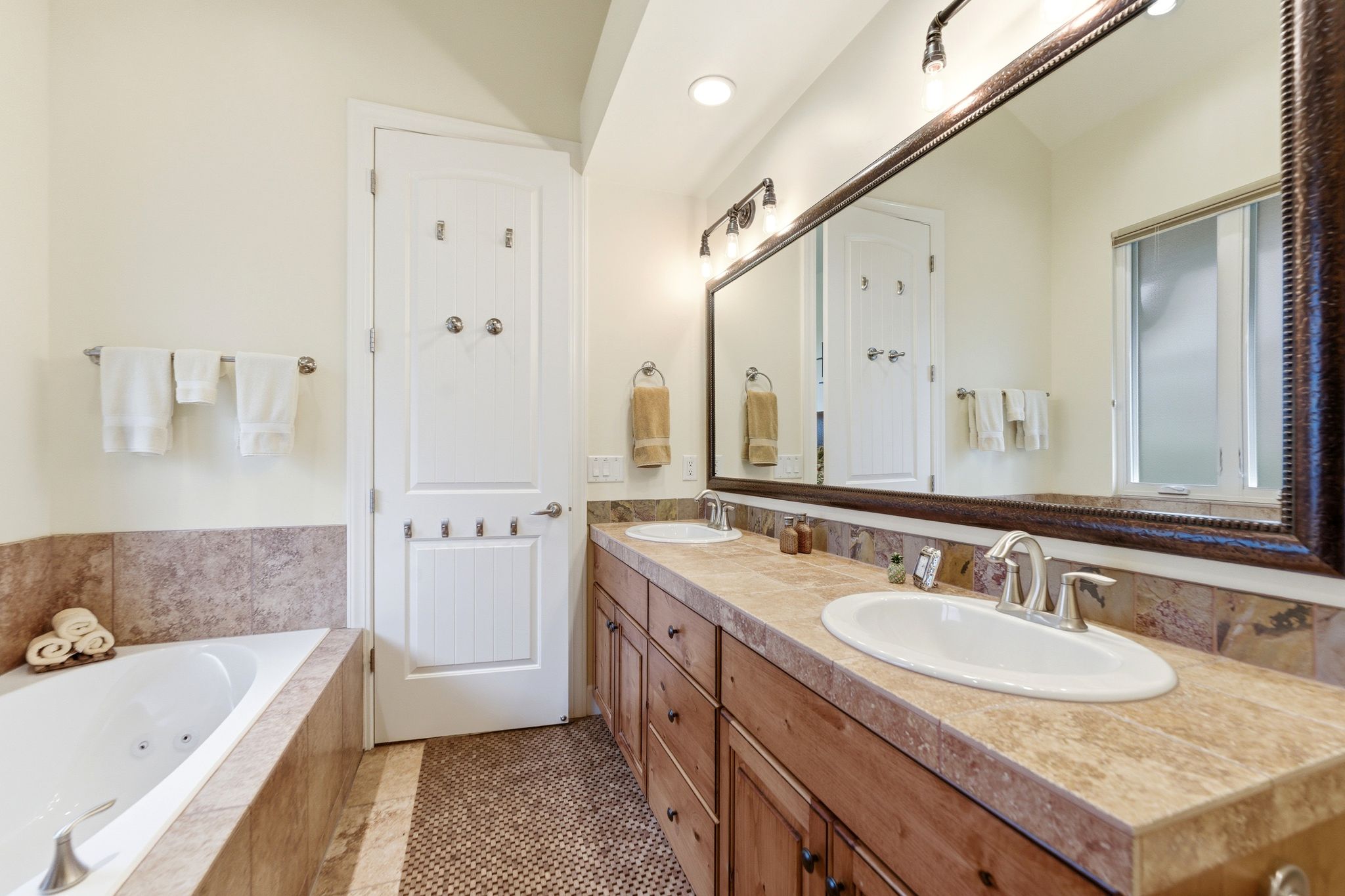 Bathroom featuring a soaking tub, a double vanity with integrated sinks, wood cabinetry, and a large framed mirror
