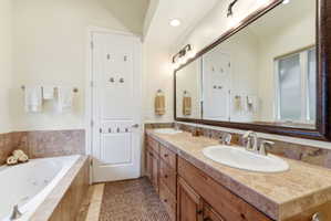Bathroom featuring a soaking tub, a double vanity with integrated sinks, wood cabinetry, and a large framed mirror